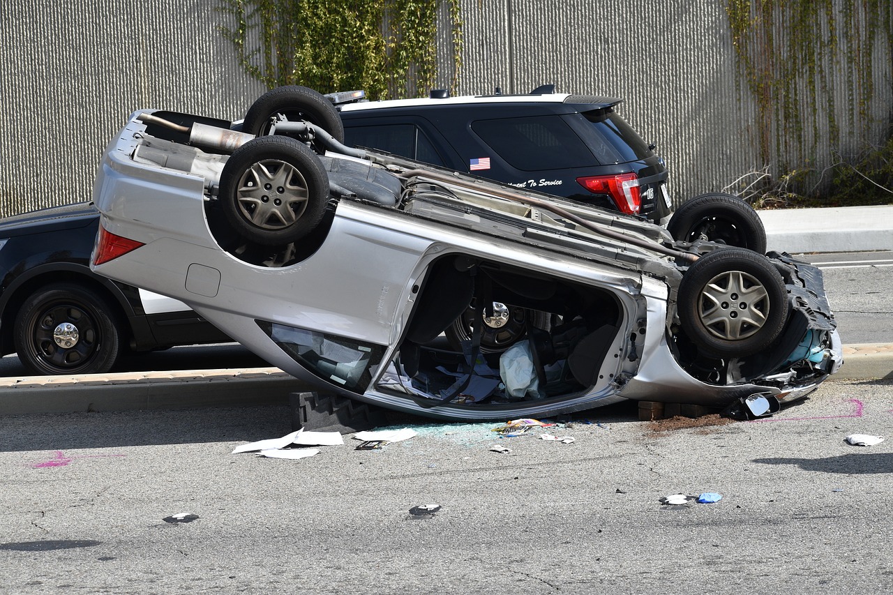 A person standing next to their car after a car accident, talking on the phone.