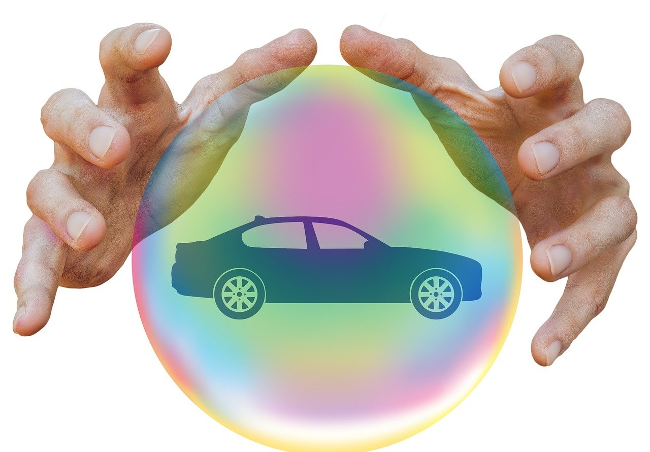 A car driving on a road with a shield icon overlay representing insurance coverage.